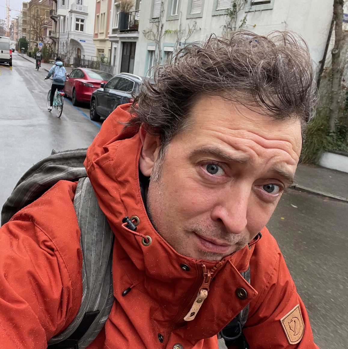A picture of Gilles Dutilh on a bicycle on a rainy day in a street of Basel